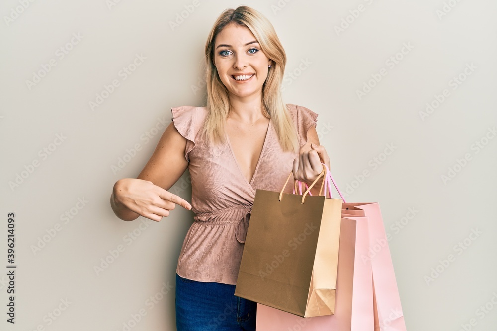 Young caucasian woman holding shopping bags smiling happy pointing with hand and finger Young caucasian woman holding shopping bags smiling happy pointing with hand and finger