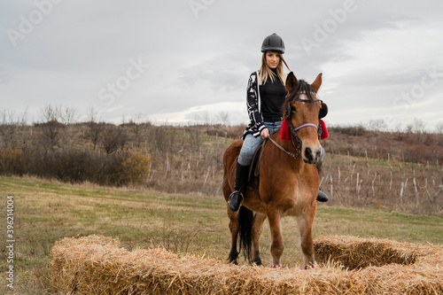 Young caucasian blonde woman female girl on the horse riding in nature wearing helmet in winter or autumn day against a cloudy sky in the field - Freedom concept copy space