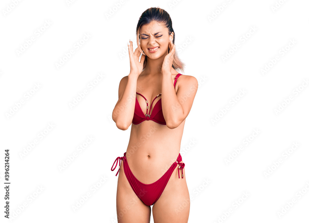 Young beautiful woman wearing bikini covering ears with fingers with annoyed expression for the noise of loud music. deaf concept. Young beautiful woman wearing bikini covering ears with fingers with annoyed expression for the noise of loud music. deaf concept.