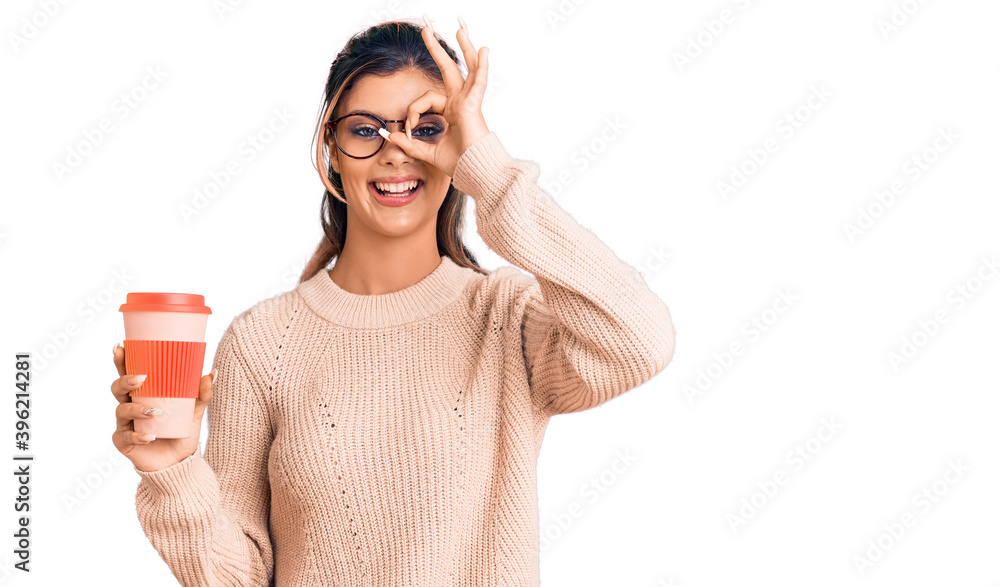 Young beautiful woman wearing glasses holding takeaway cup of coffee smiling happy doing ok sign with hand on eye looking through fingers Young beautiful woman wearing glasses holding takeaway cup of coffee smiling happy doing ok sign with hand on eye looking through fingers