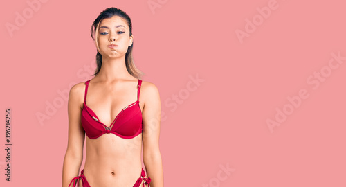 Young beautiful woman wearing bikini puffing cheeks with funny face. mouth inflated with air, crazy expression.