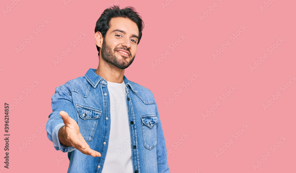 Young hispanic man wearing casual clothes smiling cheerful offering palm hand giving assistance and acceptance. Young hispanic man wearing casual clothes smiling cheerful offering palm hand giving assistance and acceptance.