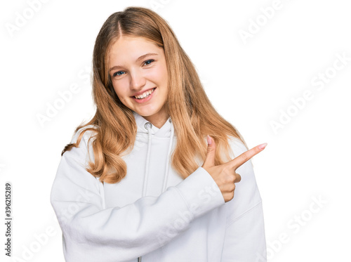 Beautiful young caucasian girl wearing casual sweatshirt cheerful with a smile of face pointing with hand and finger up to the side with happy and natural expression on face
