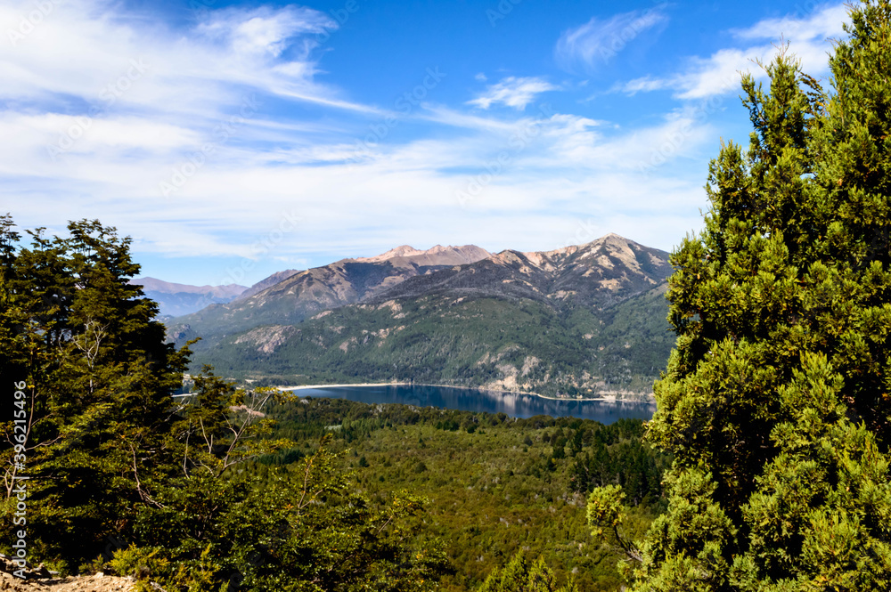 Wonderful lake landscape between the mountains with pine trees and rocks on a very sunny day on a hill in Bariloche, Argentina