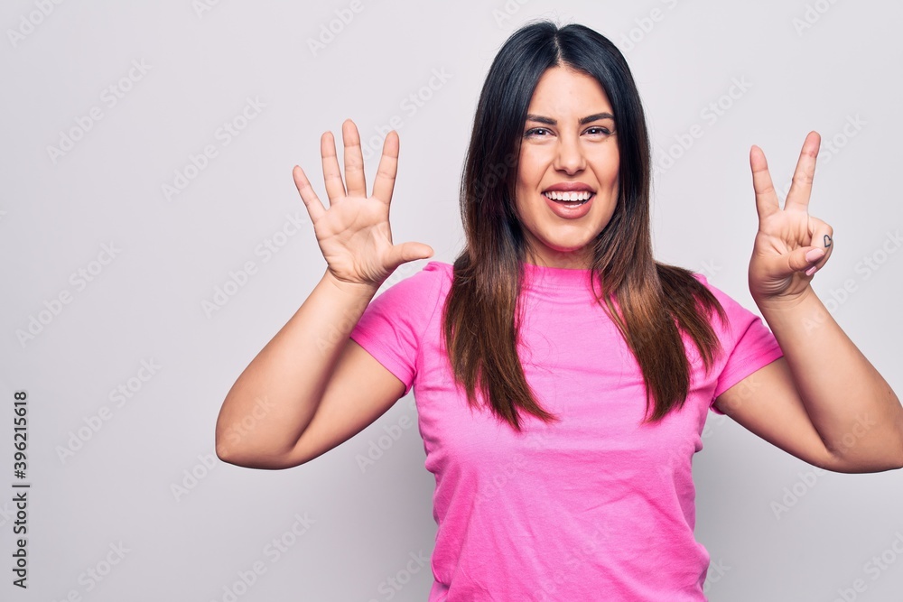 Young beautiful brunette woman wearing casual pink t-shirt standing over white background showing and pointing up with fingers number seven while smiling confident and happy. Young beautiful brunette woman wearing casual pink t-shirt standing over white background showing and pointing up with fingers number seven while smiling confident and happy.