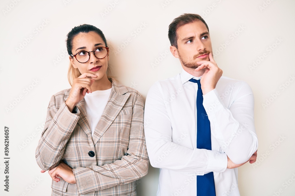 Beautiful couple wearing business clothes with hand on chin thinking about question, pensive expression. smiling with thoughtful face. doubt concept. Beautiful couple wearing business clothes with hand on chin thinking about question, pensive expression. smiling with thoughtful face. doubt concept.