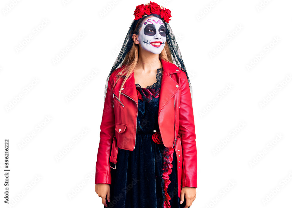 Woman wearing day of the dead costume over background looking away to side with smile on face, natural expression. laughing confident.