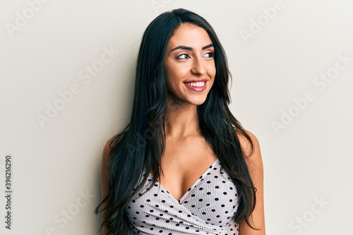 Beautiful hispanic woman wearing casual clothes looking away to side with smile on face, natural expression. laughing confident.