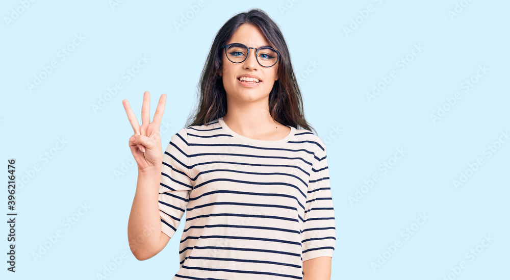 Brunette teenager girl wearing casual clothes and glasses showing and pointing up with fingers number three while smiling confident and happy.