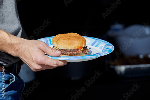 Slika na platnu Hand holding a paper plate with a Hamburger on it