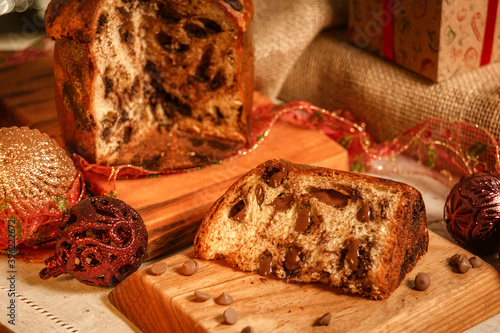 Slice of chocolate panettone  on wooden cutting board with christmas ornaments photo