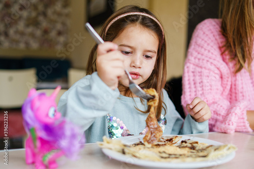 Wallpaper Mural Front view on small caucasian girl eating pancakes desert at restaurant - little child female kid having breakfast meal at by the table at home in day - growing up and eating food concept Torontodigital.ca