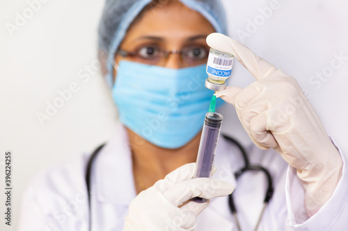 Indian doctor draws medication into an injection syringe from a vaccine bottle 