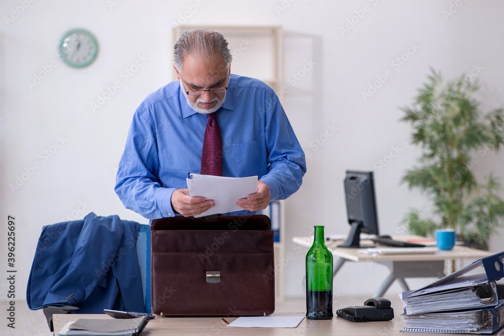 Old male employee drinking alcohol in the office Old male employee drinking alcohol in the office