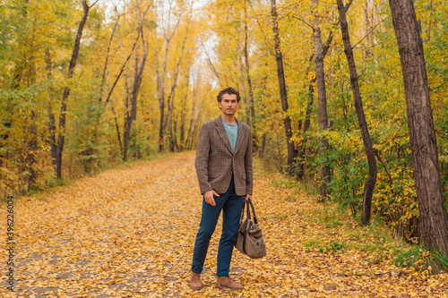 Tall handsome man with a bag on the autumn alley