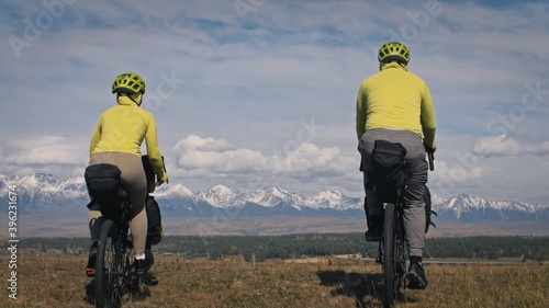 Fototapeta Naklejka Na Ścianę i Meble -  The man and woman travel on mixed terrain cycle touring with bikepacking. The two people journey with bicycle bags. Mountain snow capped.