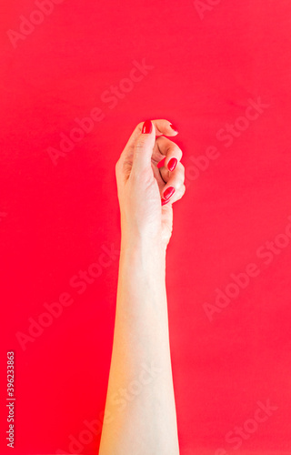 Female hand on a red background. Red manicure. The photo was taken with selective focus and has a noise effect.