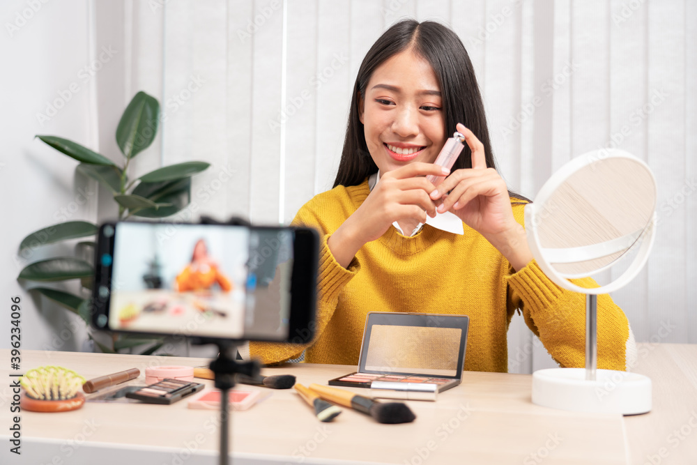 Beautiful asian woman blogger using camera phone recording vlog video live streaming and applying makeup for review cosmetics at home