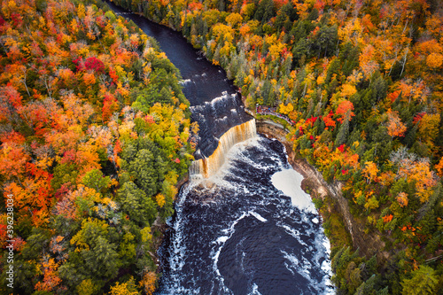 Incredible aerial photograph of the upper waterfall cascade at Tahquamenon Falls with beautiful autumn foliage on the trees with green, yellow, red and orange leaves surrounding the river.