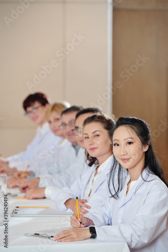 Group of researchers taking notes when attending meeting in boardroom and looking at camera