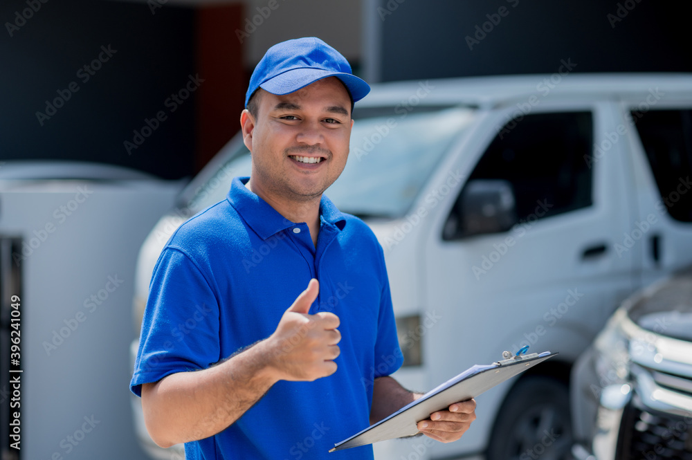 A car maintenance worker standing with thumbs up while holding clipboard checking a list of items for car maintenance for a workshop customer.