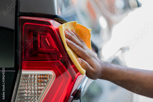 The car polisher uses a microfiber cloth and polish to wipe the car's tail lights to make them shine He takes care of every detail of the car. photo