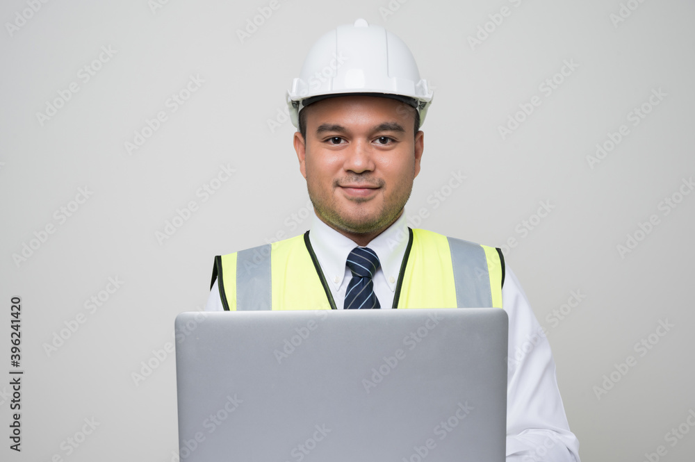 Asian civil engineer operate with laptop to control working in studio. Worker wearing hard hat using laptop computer standing on isolated white background. Asian civil engineer operate with laptop to control working in studio. Worker wearing hard hat using laptop computer standing on isolated white background.