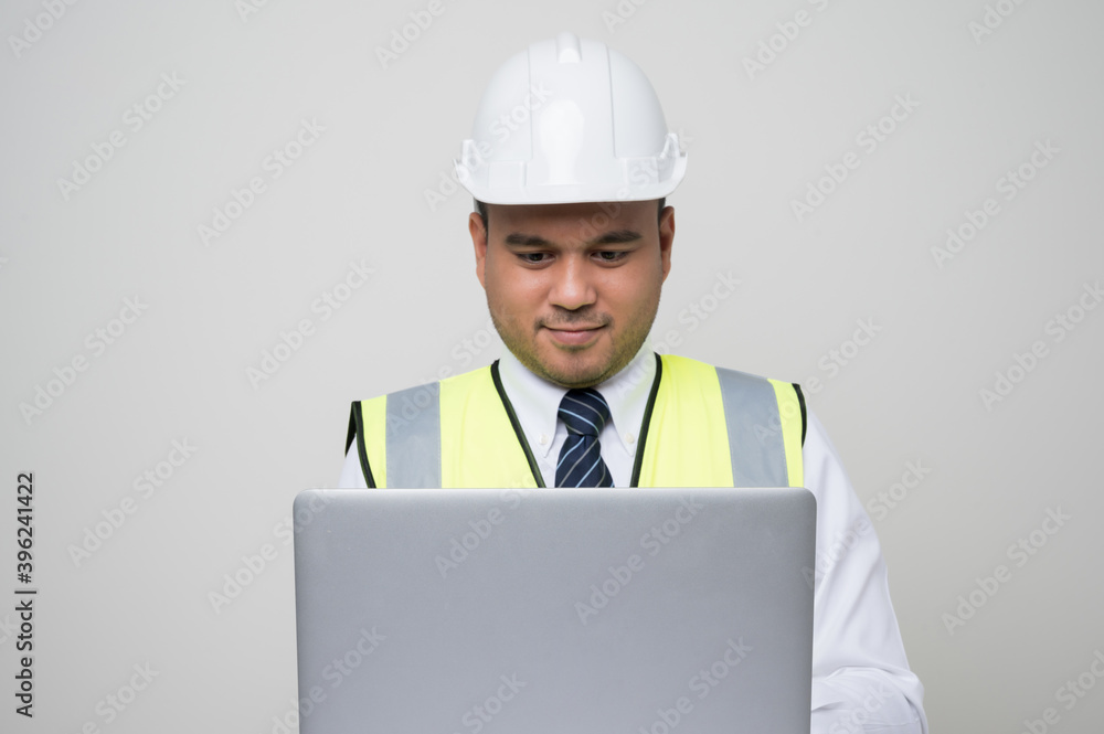 Asian civil engineer operate with laptop to control working in studio. Worker wearing hard hat using laptop computer standing on isolated white background. Asian civil engineer operate with laptop to control working in studio. Worker wearing hard hat using laptop computer standing on isolated white background.