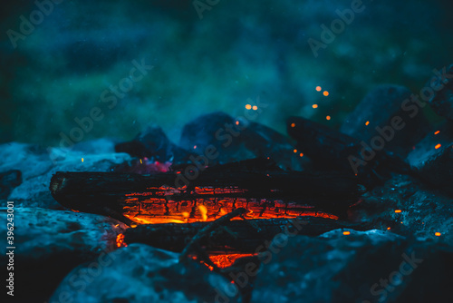 Vivid smoldered firewoods burned in fire close-up. Atmospheric warm background with orange flame of campfire and blue smoke. Wonderful full frame image of bonfire. Burning logs in beautiful fire. © Daniil