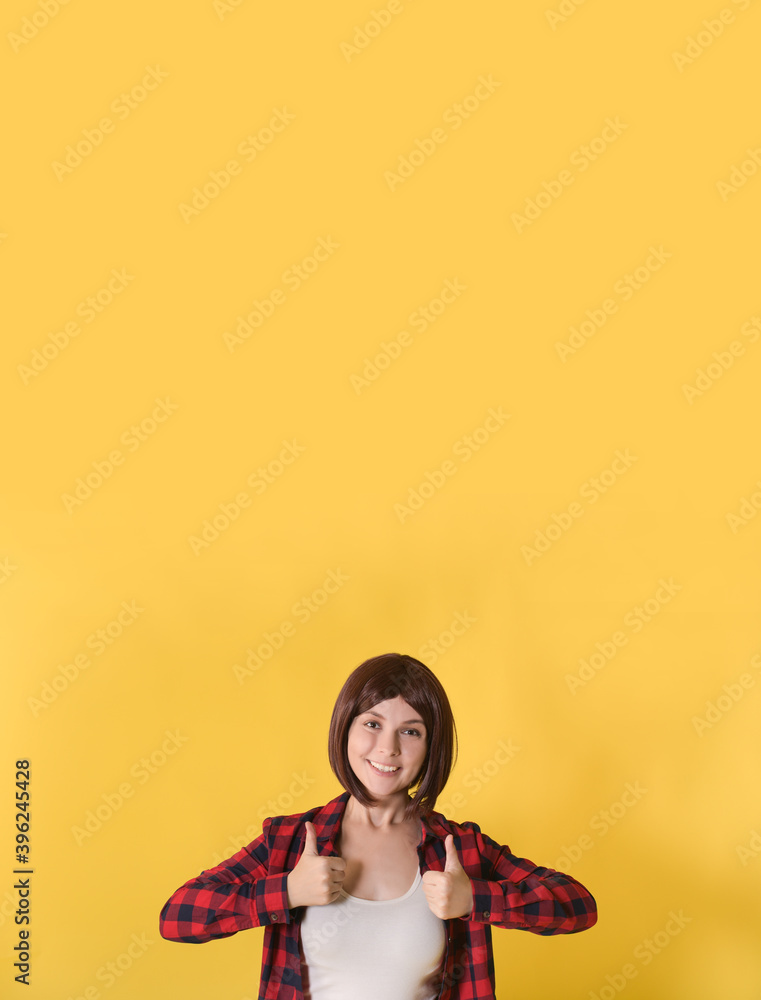 Portrait beautiful young woman standing in checked shirt and gave thumbs up: vertical banner with space for text, well signed sign and looking at the camera on yellow background