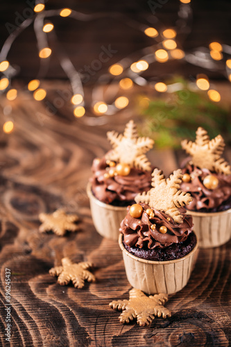 Chocolate cupcakes with star shaped cookies on a wooden background. Christmas mood. Sweets for any occasion. In the background are yellow lights from the garland