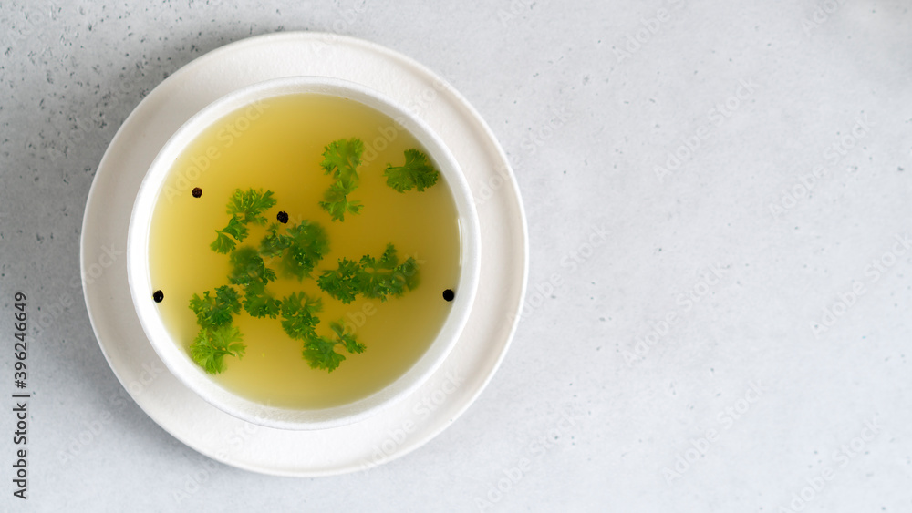 Homemade beef bone broth in white bowl with parsley leaves and peppercorns. Health benefits. Collagen is good for joints. Flat lay. Copy space. Homemade beef bone broth in white bowl with parsley leaves and peppercorns. Health benefits. Collagen is good for joints. Flat lay. Copy space.