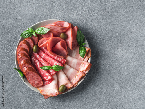 Antipasto set platter on plate over gray stone. Cold smoked meat plate with sausage,sliced ham,prosciutto, bacon, olives and basil. Appetizer variety with copy space. Top view or flat lay.