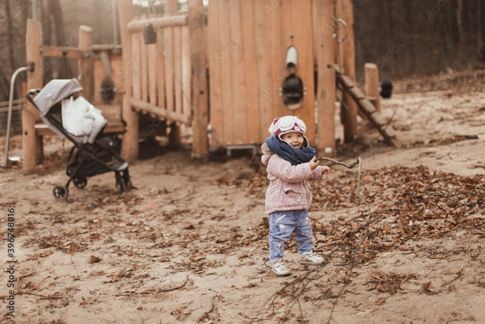Cute cute little girl child toddler in a snood and a hat walks on the playground autumn in the park, brown toning