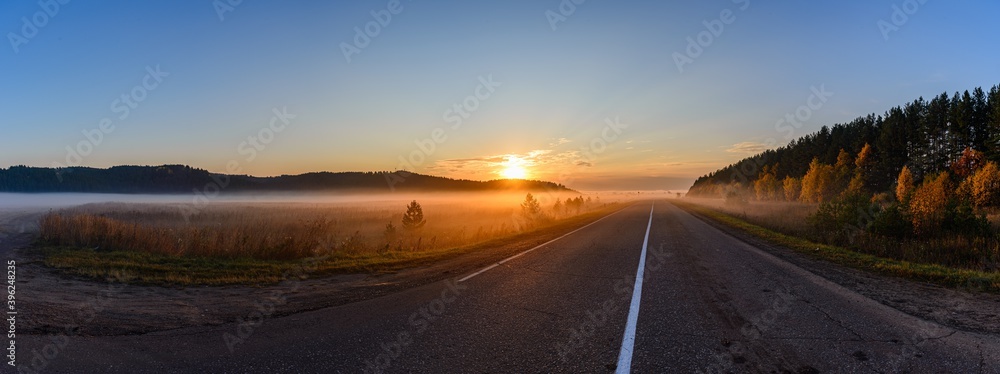 Sunrise, in the foreground the road passing through the field is covered with a thin layer of fog