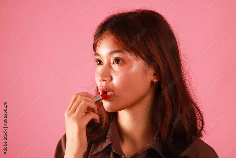 Portrait of young girl painting her lips with bright lipstick on pink background. Portrait of young girl painting her lips with bright lipstick on pink background.