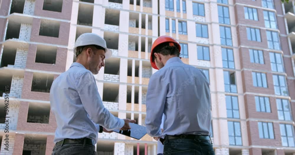 The engineer shakes hands with the chief builder and shows him the drawings on the tablet, then focuses on the paper drawings and points to the construction site. The engineer shakes hands with the chief builder and shows him the drawings on the tablet, then focuses on the paper drawings and points to the construction site.
