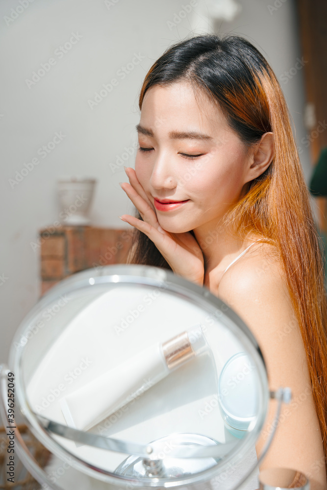 Asian woman applying cream lotion on her face in natural light. Asian woman applying cream lotion on her face in natural light.
