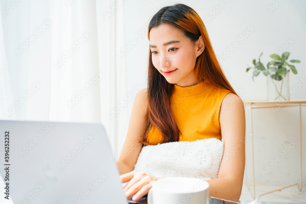 Asian woman working on laptop computer in white room.
