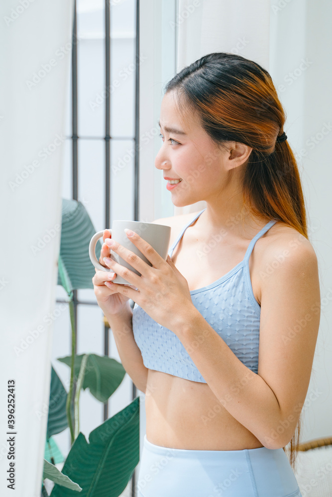 Beautiful sporty asian woman holding cup of coffee looking outside the window. Beautiful sporty asian woman holding cup of coffee looking outside the window.