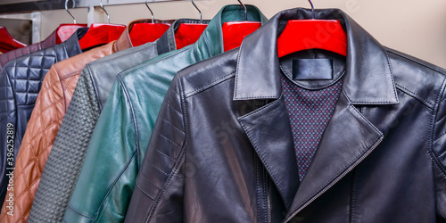 Male black and crown clothes on a hanger in a store. New collection of different color spring leather jackets for men.