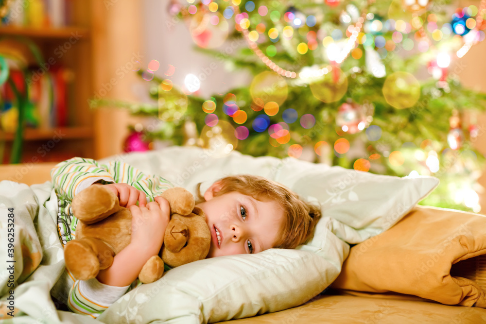 Little cute blond boy sleeping under Christmas tree and dreaming of Santa at home, indoors. Traditional Christian festival. Happy kid child waiting for gifts on xmas. Cozy soft light Little cute blond boy sleeping under Christmas tree and dreaming of Santa at home, indoors. Traditional Christian festival. Happy kid child waiting for gifts on xmas. Cozy soft light