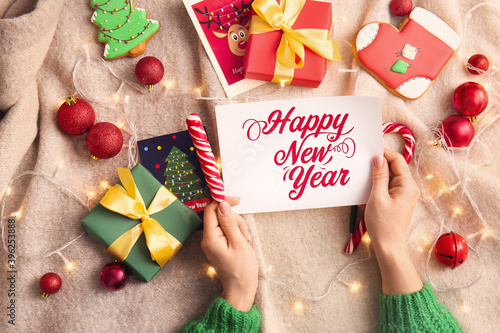 Woman with greeting postcard for New Year celebration and gifts on bed