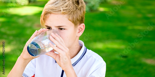 Young caucasian boy drinking fresh mineral water, outdoors, summer time. Health concept. Water filters, clear water.