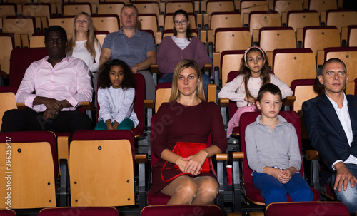 Father, mom and daughter are carefully watching spectacle or concert in the theater auditorium