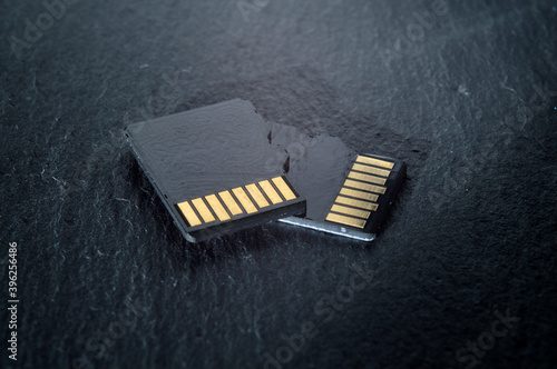 two micro sd cards lie on top of each other on a dark textured background, with golden contacts at the top. close-up.