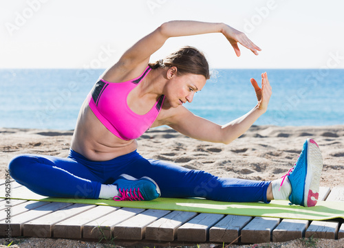 Fototapeta Naklejka Na Ścianę i Meble -  Ordinary healthy female stretching muscles on the sand