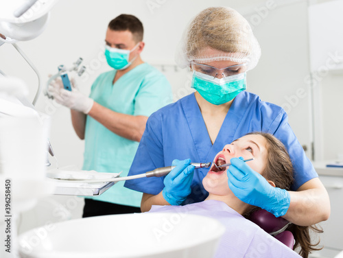 Professional female dentist performing treatment for teenage girl with male assistant behind