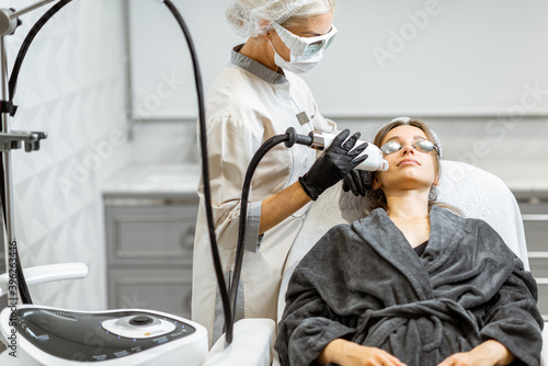 Professional doctor in protective wear making a laser rejuvenation treatment for a young woman client at medical office. LaseMD procedure