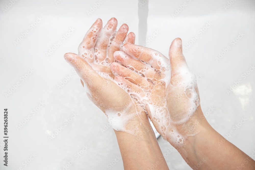 Fototapeta premium Close up a woman is washing soap foam from her hands under running water.